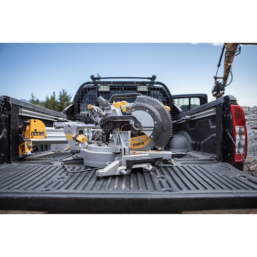 DEWALT miter saw placed in the bed of a black pickup truck at an outdoor construction site.