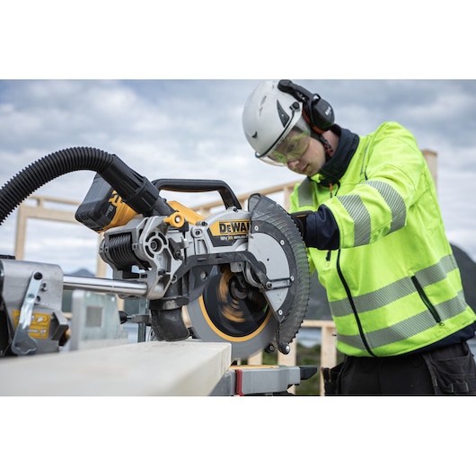 Person using a DEWALT DCS782N mitre saw outdoors, wearing safety gear and cutting wood.