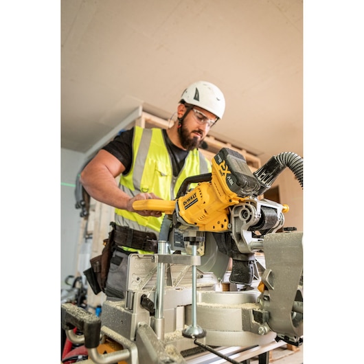 Worker uses yellow DEWALT DCS782N saw on construction site, wearing high-visibility vest and helmet.