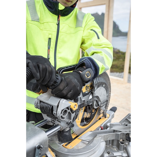 Person in high-visibility jacket operating a DEWALT miter saw outdoors.
