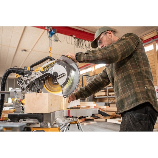 DEWALT DCS782N saw cutting wood in workshop with worker handling machine.