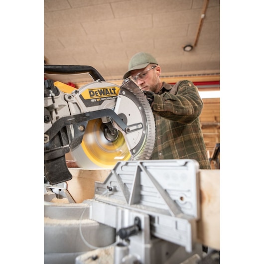 DEWALT DCS782N mitre saw cutting wood, operated by a person in a workshop.