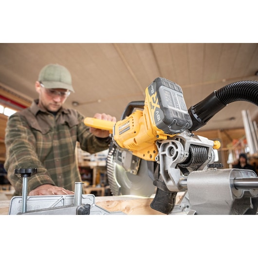 DEWALT DCS782N saw cutting wood in workshop, operated by person in plaid shirt. Close-up of tool and battery.