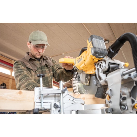 Person using a DEWALT DCS782N saw to cut wood in a workshop setting.