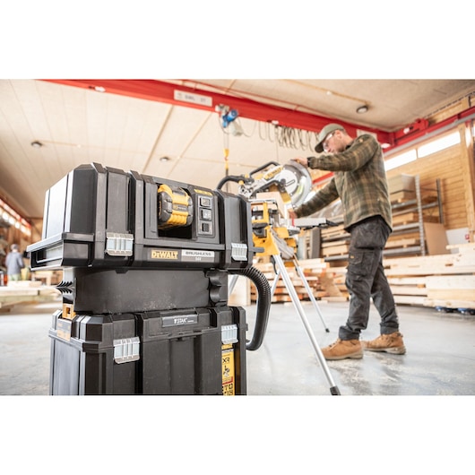 DEWALT DCS782N equipment in a workshop, with a worker operating a saw and wooden materials in the background.