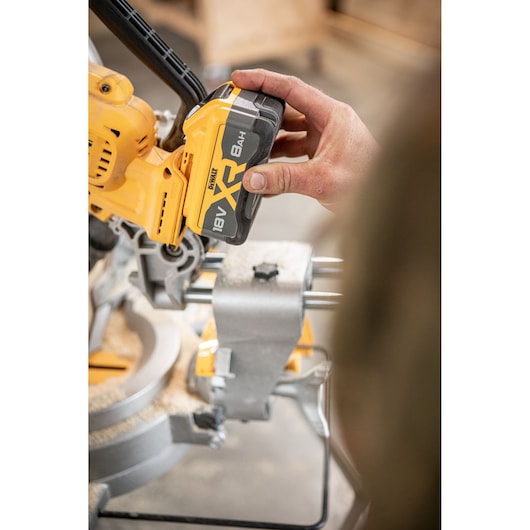 Hand inserts DEWALT 18V XR battery into yellow power tool in workshop setting.