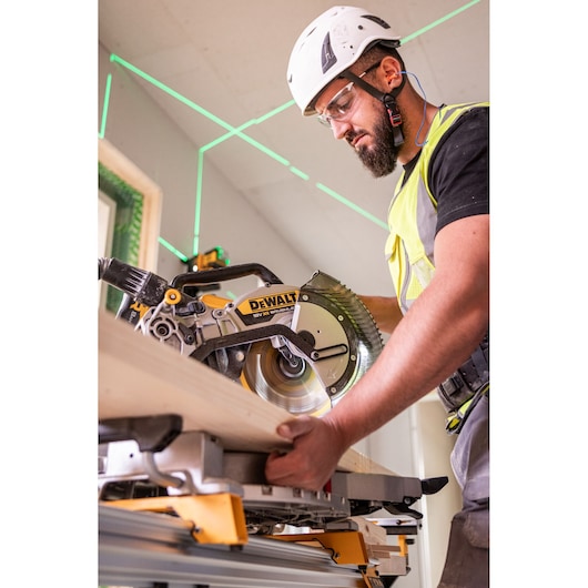 Worker uses DEWALT DCS782N saw to cut wood indoors, wearing safety gear and helmet.