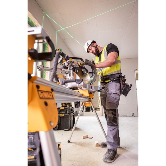 Worker uses DEWALT miter saw DCS782N with safety gear in an indoor construction site.