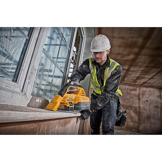 A construction worker wearing a safety helmet and reflective vest is using a DEWALT DCV517N portable vacuum cleaner to clean