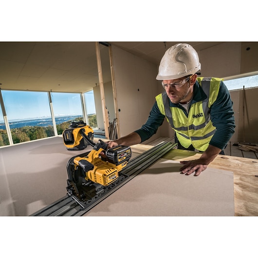 A construction worker wearing a safety helmet and a high-visibility DEWALT vest operates a yellow DEWALT cordless power