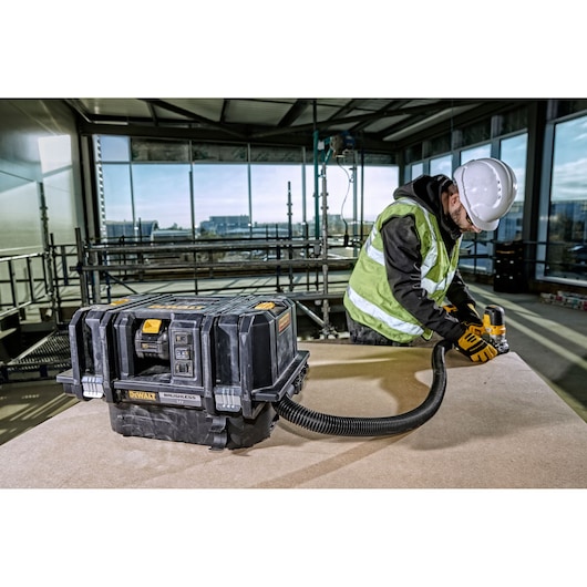A DEWALT brushless portable dust extractor (model DCV586MT2) is placed on a work table at a construction site. A worker