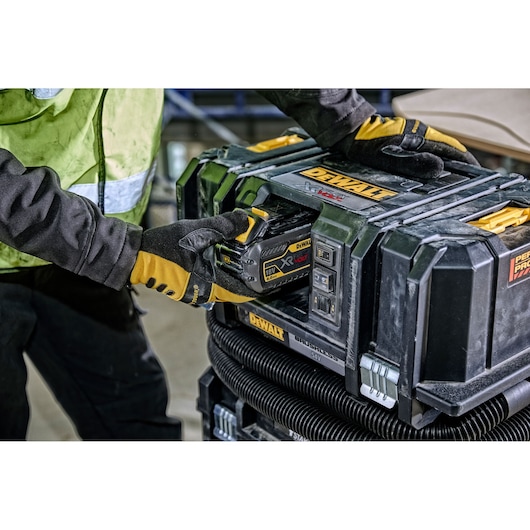A person wearing work gloves is inserting a DEWALT XR FLEXVOLT 18V battery into a DEWALT portable power tool case at a