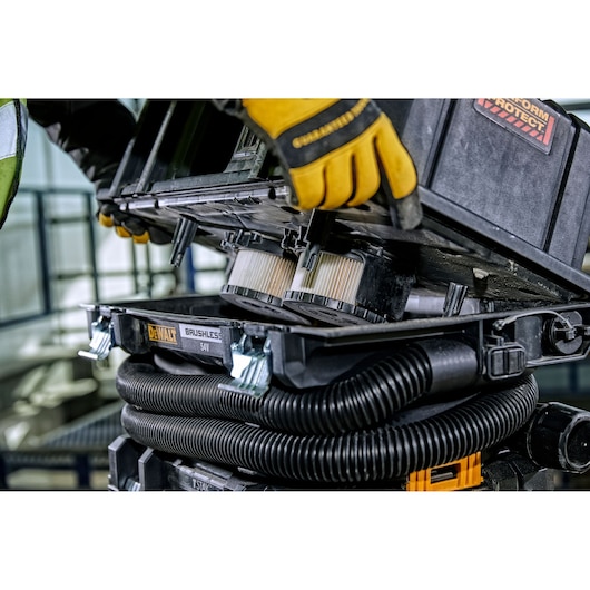 Close-up of a DEWALT brushless 54V portable vacuum cleaner, showing a person wearing yellow work gloves opening the unit to