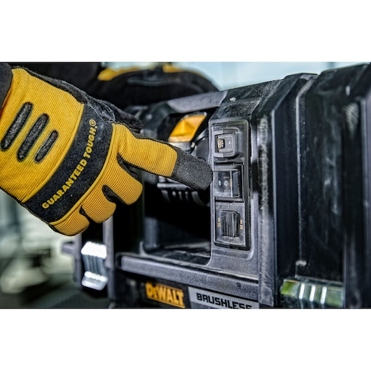 A close-up of a gloved hand pressing a button on a DEWALT brushless power tool with visible dust and control switches.