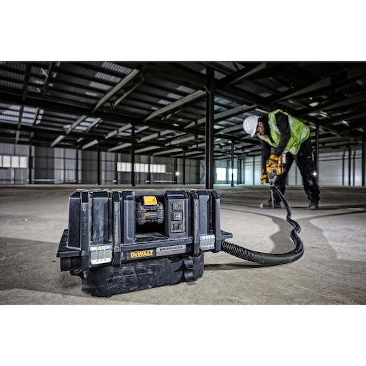 A DEWALT DCV586MT2 brushless vacuum cleaner is placed on the floor of a large industrial building under construction. A