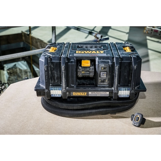 A DEWALT 54V brushless portable dust extractor with a hose and remote control, placed on a work surface in a construction