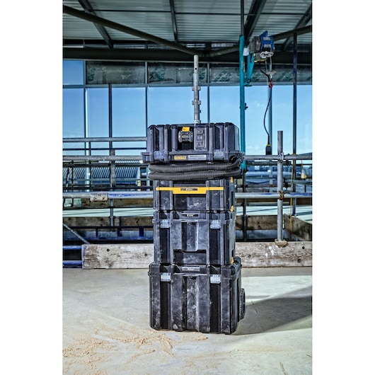 A stack of DEWALT ToughSystem storage boxes with a DCV586MT2 cordless dust extractor on top, situated in an industrial