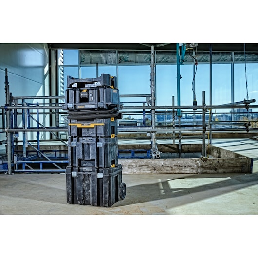 Stacked DEWALT black and yellow tool storage boxes with wheels are placed on a construction site floor. Scaffolding and a