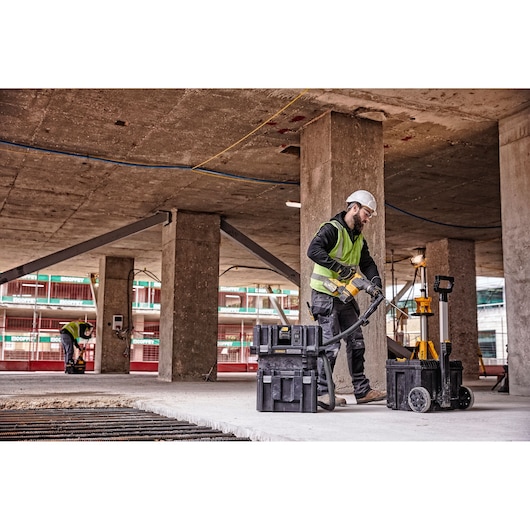 A person wearing a safety vest and helmet operates a DEWALT vacuum cleaner and tool kit on a construction site with concrete