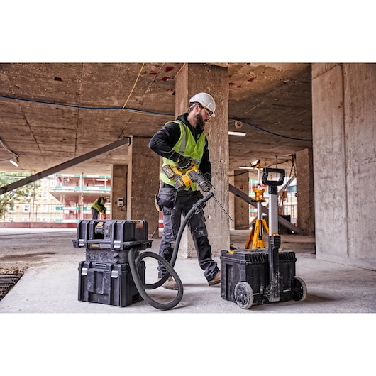 A construction worker wearing a high-visibility vest and a hard hat uses a DEWALT power tool connected to a vacuum system