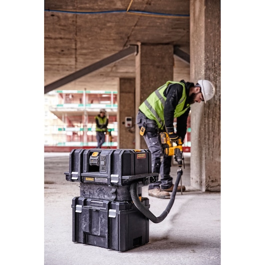 A DEWALT DCV586MT2 portable vacuum and tool storage unit is positioned on a construction site floor, with two workers in