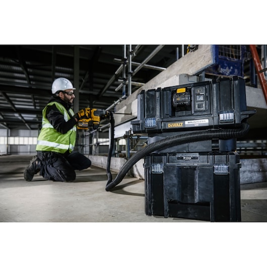A DEWALT DCV586MT2 brushless 54V dust extractor is shown in the foreground of a construction site, with a worker wearing a