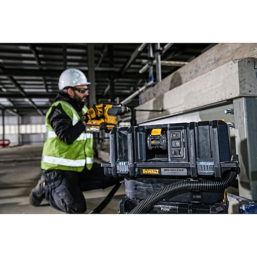 A DEWALT brushless 54V tool box is in the foreground, with a hose attached to it. In the background, a construction worker