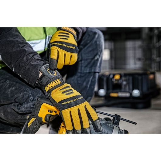 Close-up of a person wearing DEWALT branded yellow and black work gloves, adjusting the glove strap. The person is holding a