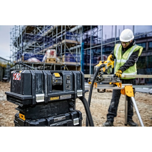 A DEWALT brushless vacuum cleaner unit (model DCV586MT2) is placed on a jobsite, with construction scaffolding in the