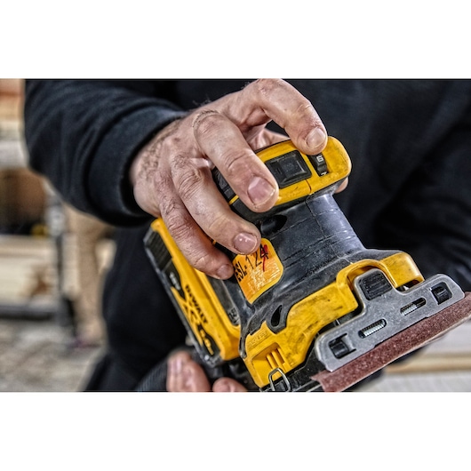 A close-up of a hand adjusting a DEWALT cordless sander, showing the speed dial and sanding pad.