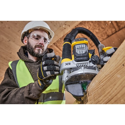 A worker wearing safety gear operates a DEWALT XR cordless router on a wooden surface, with wood shavings being produced.