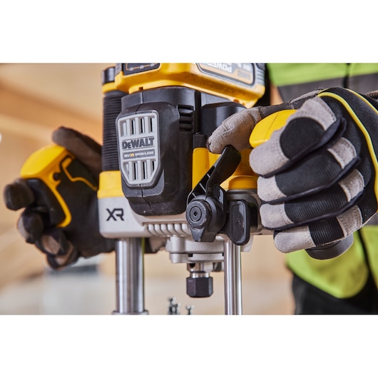 Gloved hands operate a DEWALT XR power tool, focusing on its controls and front section in a workshop setting.