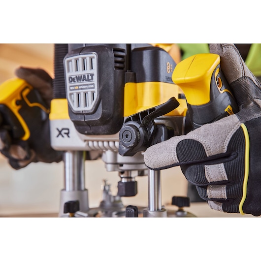 Close-up of DEWALT XR router tool, gloved hand adjusting the depth lever during use.