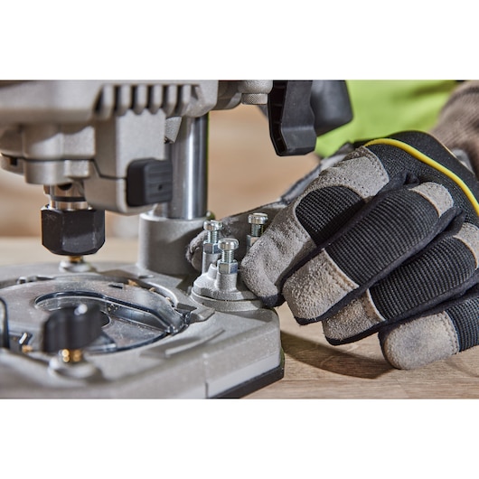 Gloved hand adjusts bolts on a DEWALT DCW620H2 power tool placed on a wooden surface.