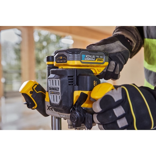 Gloved hands adjust a DEWALT cordless power tool, model DCW620NT, on a worksite with blurred background.