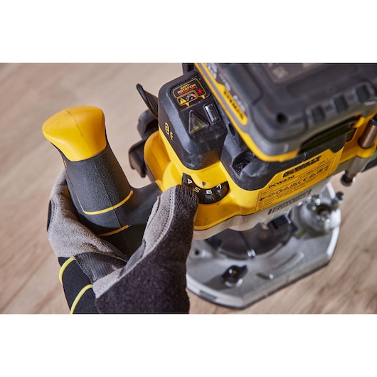 Hand adjusts speed dial on a yellow DEWALT power tool placed on a wooden surface.