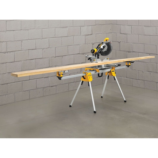 DEWALT miter saw on adjustable stand with long wooden plank in a workshop setting.