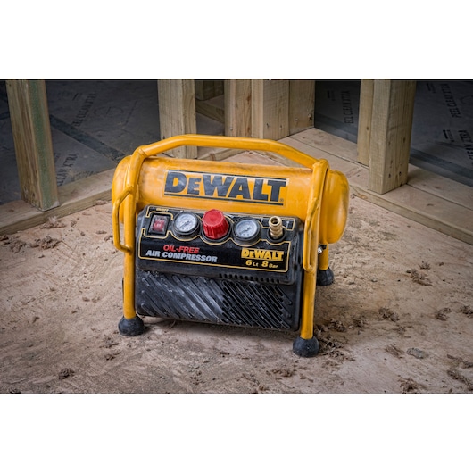 DEWALT oil-free air compressor with gauges on a construction site floor, yellow and black portable design.