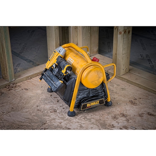 DEWALT air compressor and nail gun placed on a construction site floor near wooden framing.