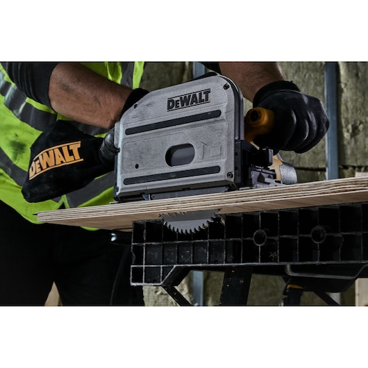 A person using a DEWALT track saw (model DT1088) to cut a wooden board, wearing gloves and a safety vest.