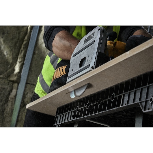 A person using a DEWALT power tool to cut a piece of wood on a workbench.