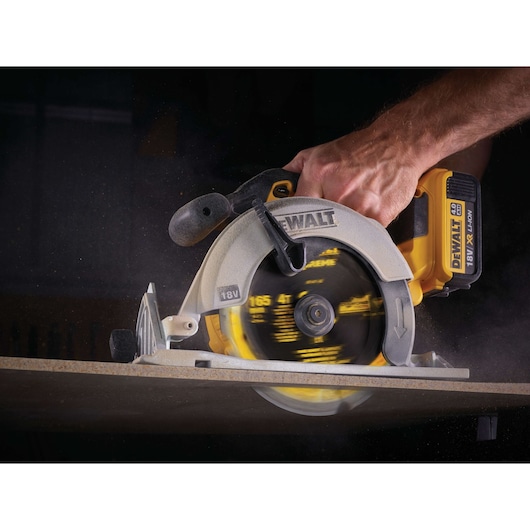 A close-up view of a person using a DEWALT 18V XR Li-Ion cordless circular saw to cut through a piece of wood.
