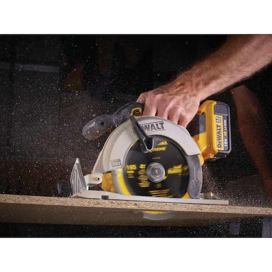 A close-up image of a DEWALT cordless circular saw being used to cut wood, showing sawdust in motion and a person's hand