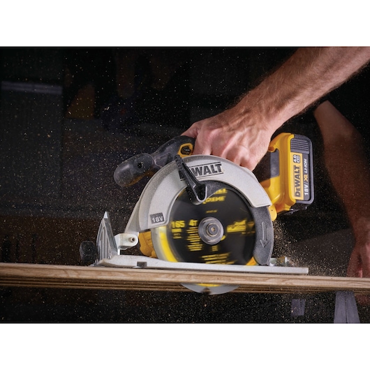 A person uses a DEWALT 18V cordless circular saw to cut through a piece of wood, with sawdust flying.