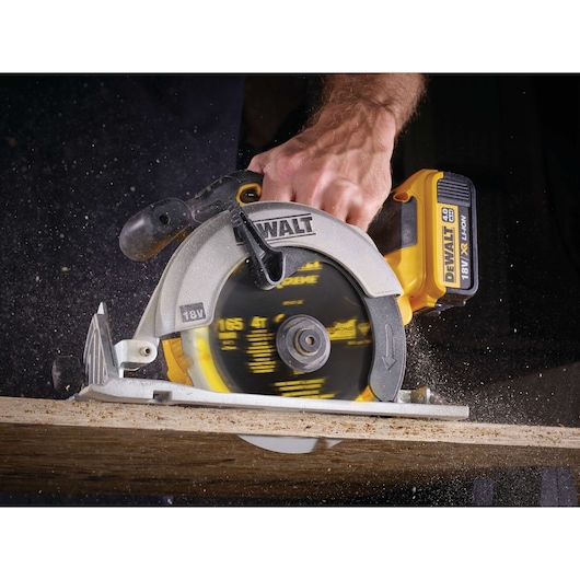 A close-up of a person using a DEWALT 18V XR Li-Ion cordless circular saw to cut through a wooden board. Sawdust is visible