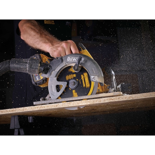 A person using a DEWALT circular saw to cut through a piece of wood, with sawdust flying around.