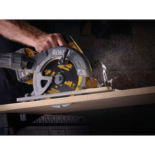 A close-up of a DEWALT circular saw cutting through a wooden board, with visible sawdust being emitted during operation.