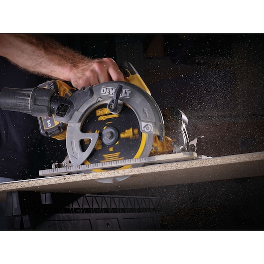 Close-up of a DEWALT circular saw in use, cutting through a piece of wood, with sawdust flying.