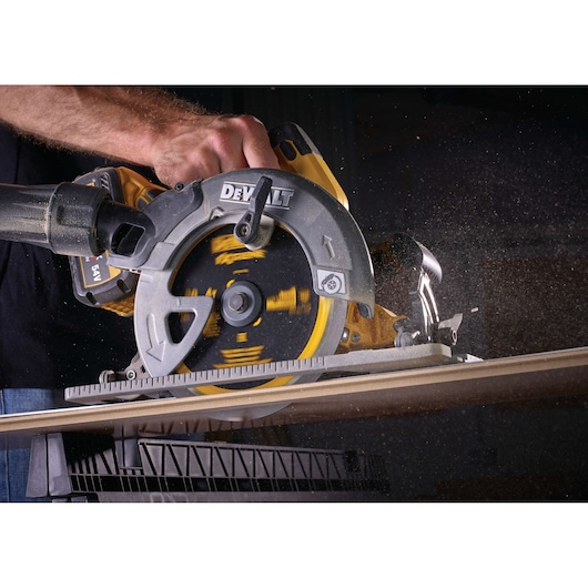 A close-up of a person using a DEWALT circular saw to cut through a wooden board, with sawdust flying in the air.