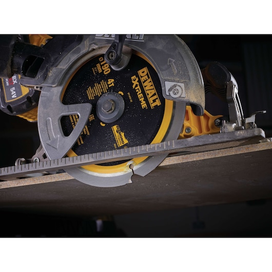 Close-up of a DEWALT circular saw blade cutting a thick piece of material in a workshop setting.